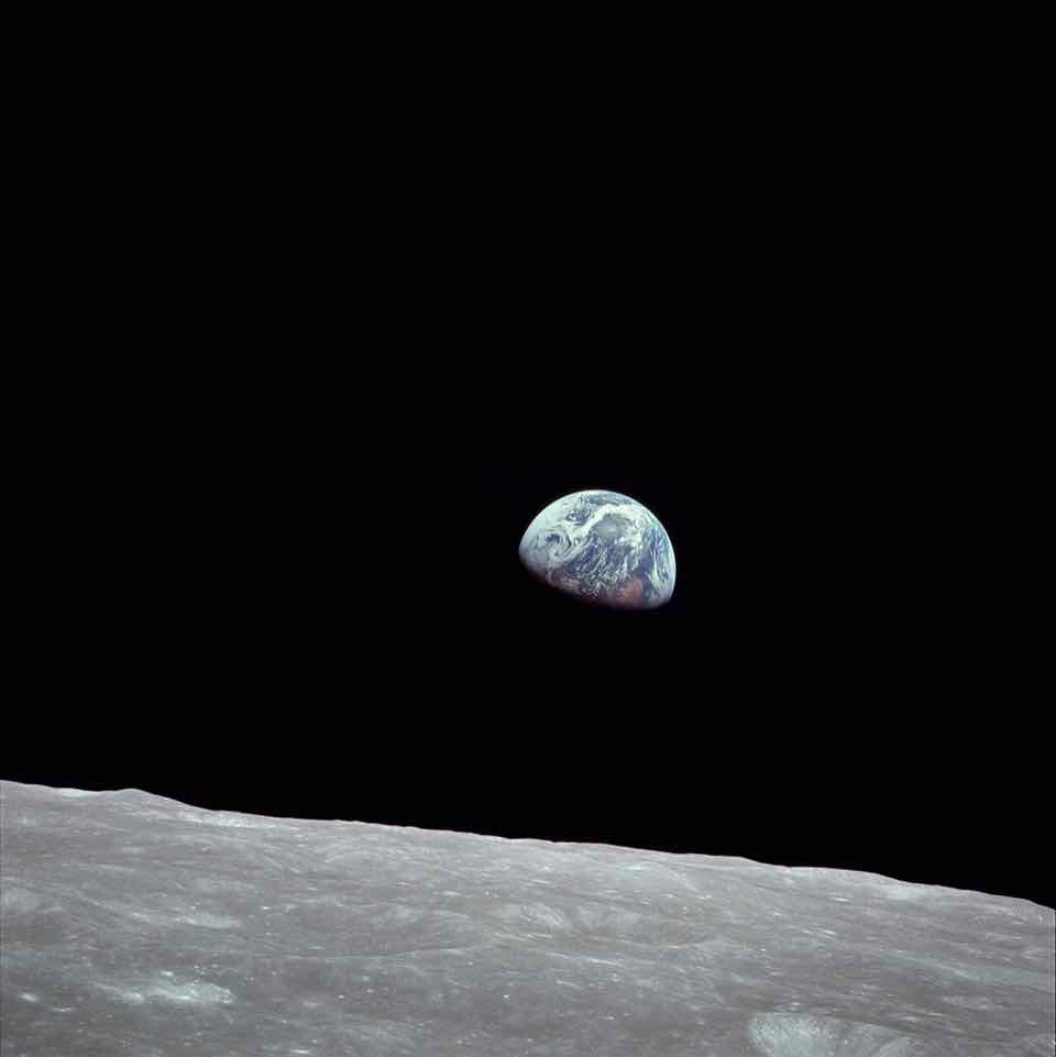 The Earth, half lit, rising over the grey horizon of the Moon.